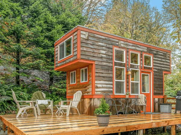 Wooden tiny home on a deck with trees behind it